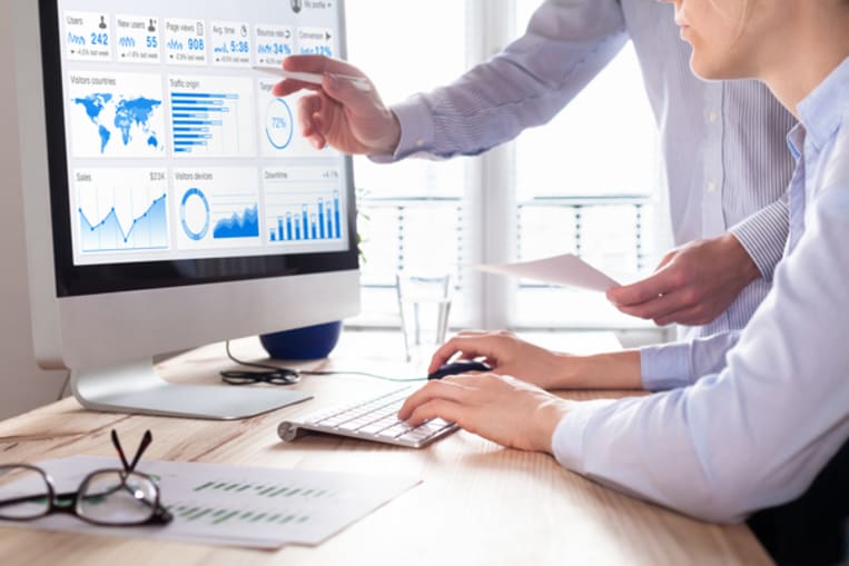 men sitting at desktop computer pointing to computer screen with graphs