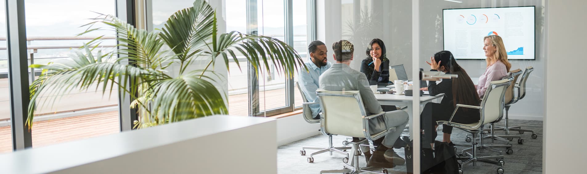 Wide angle shot of a multiracial team of male and female entrepreneurs sitting in a glass-walled meeting room of a chic office.