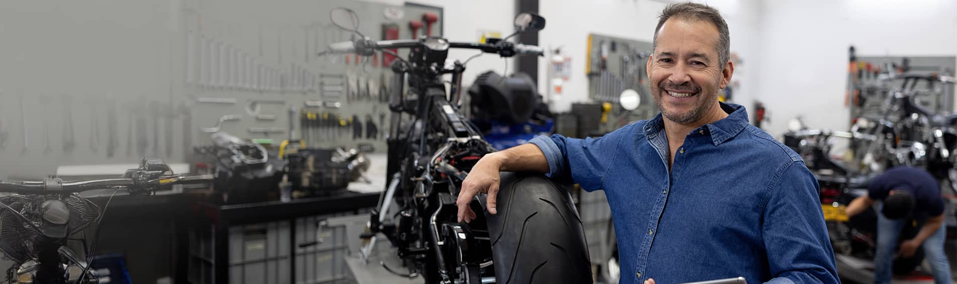 Portrait of a Latin American business owner smiling at a motorcycle repair shop and using a digital tablet